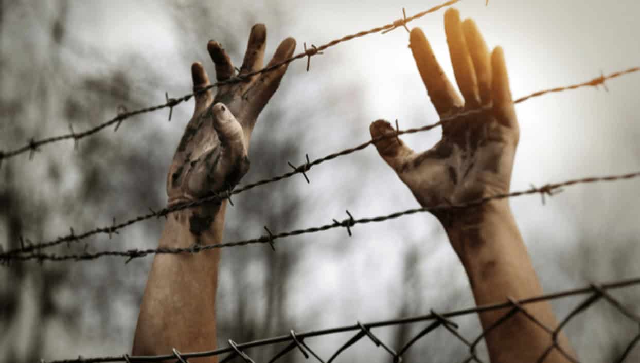 Barbed wire prison hands and dirt-covered hands reaching through a fence.