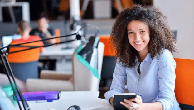 Young woman smiling at her computer in a modern classroom environment, representing tech career training and computer education at MyComputerCareer.