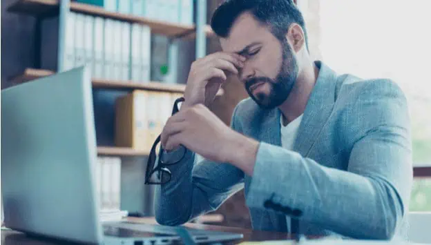 Stressful man with glasses holding his head in front of a laptop during technical training or career development at MyComputerCareer.