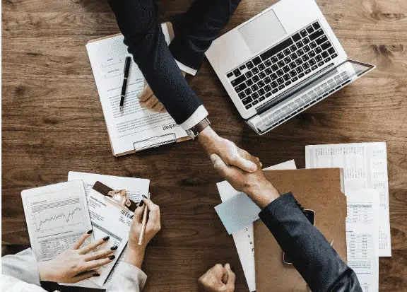 A deal with a handshake over a desk with papers.