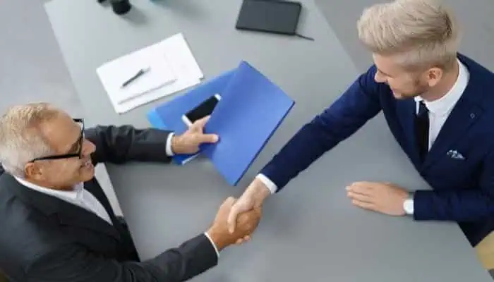 Hands-shaking business handshake between two professionals at a conference table, symbolizing career opportunities and success in technology careers.