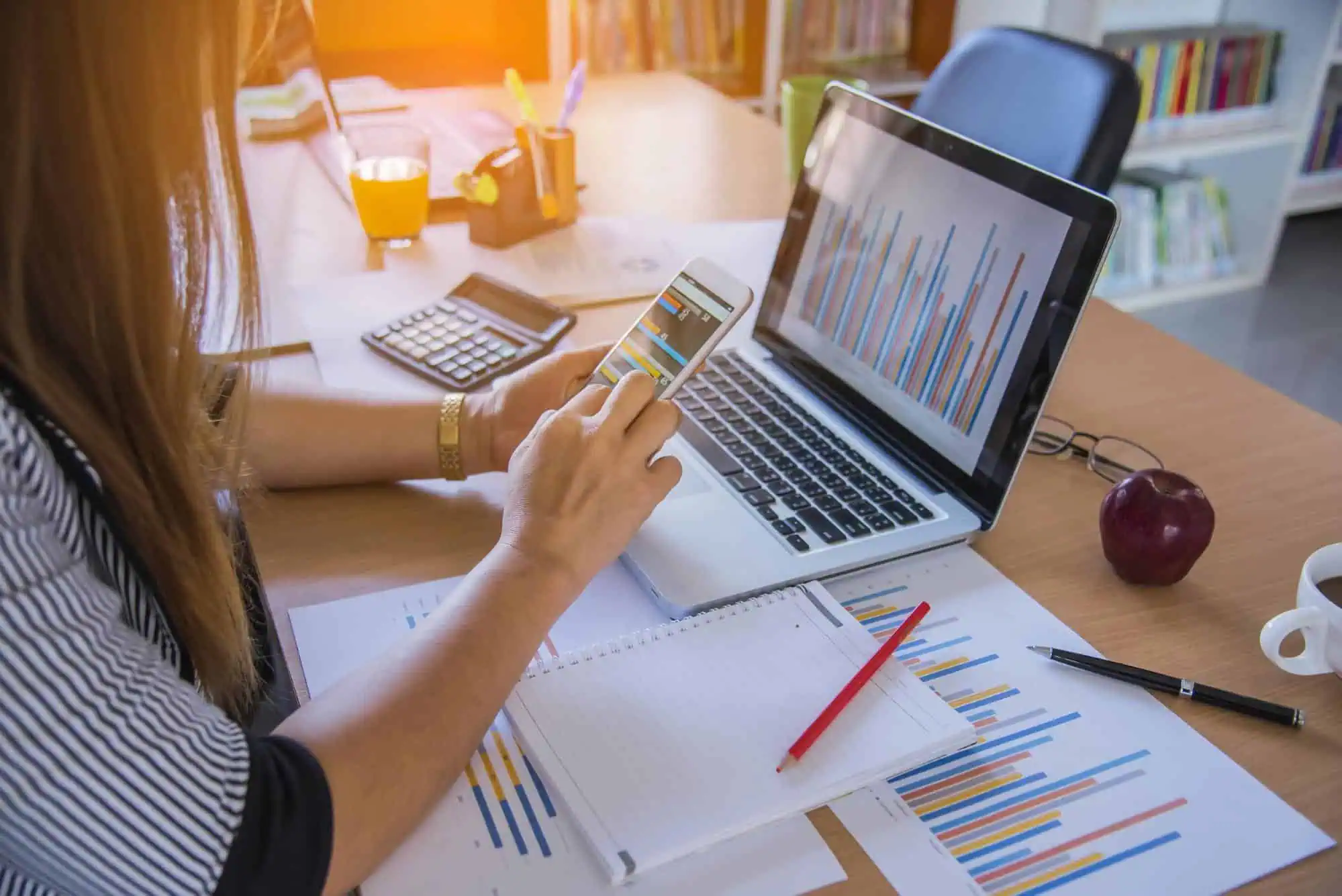 Detailed visual showing a woman analyzing data on her smartphone and laptop, surrounded by charts and office supplies, representing IT education and tech career preparation at MyComputerCareer.