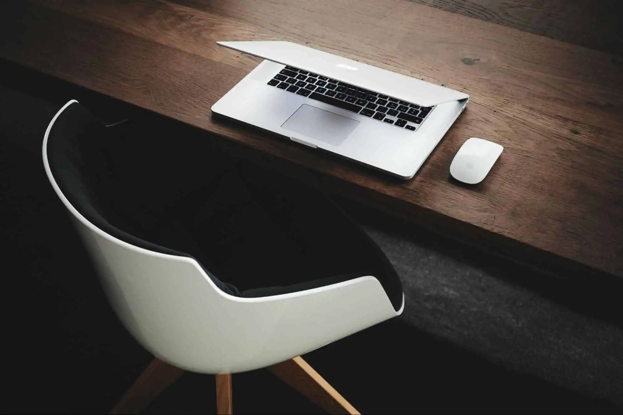 Modern Apple MacBook laptop on a wooden desk with wireless mouse in a professional workspace.