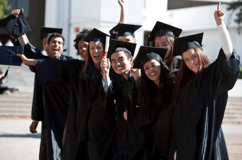 Graduates celebrating their IT and career training success in caps and gowns outside a modern building.