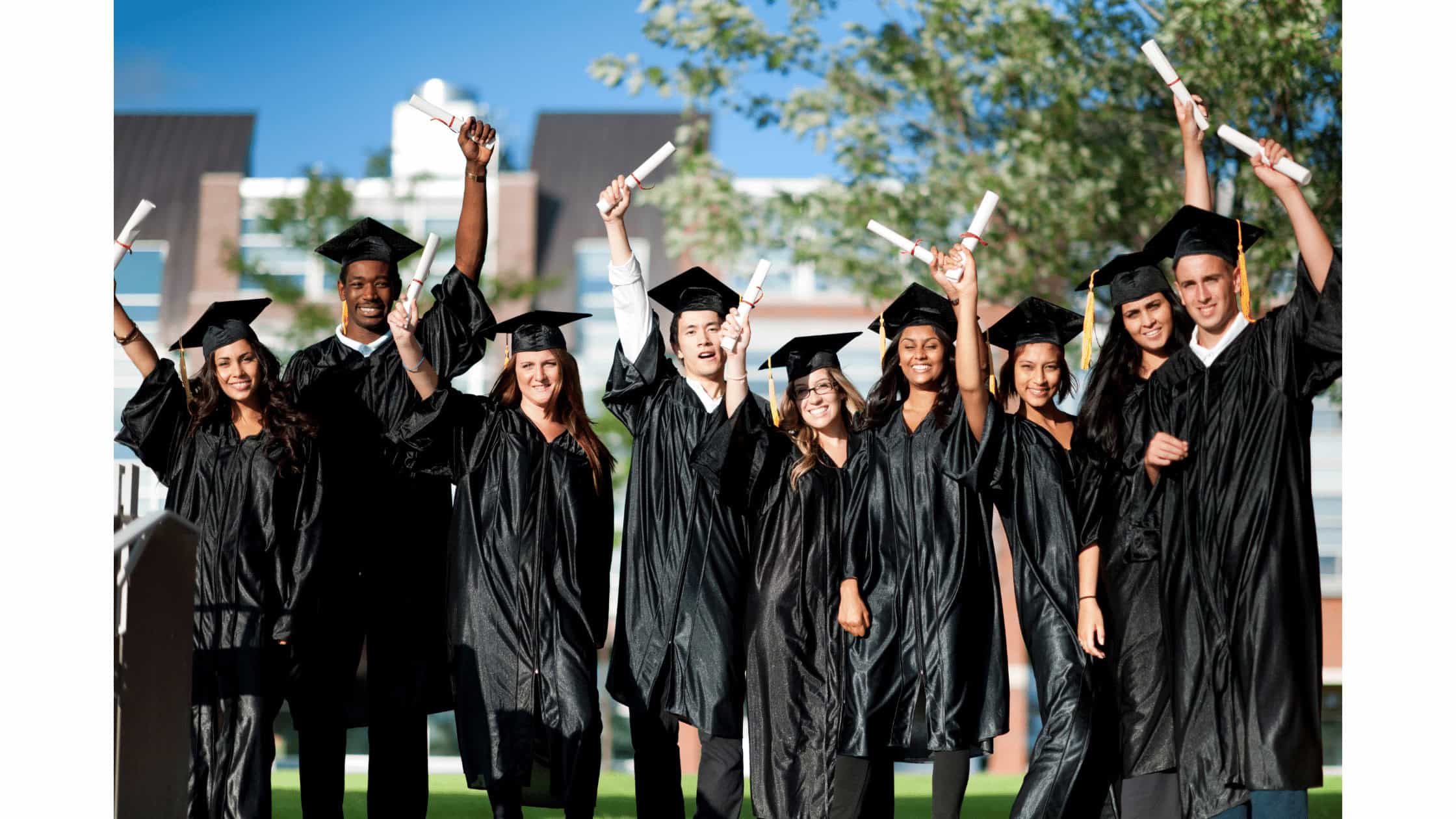 Graduating students celebrating outdoors in traditional black caps and gowns, holding diplomas, under a bright sky, representing success in computer career training and educational achievement.