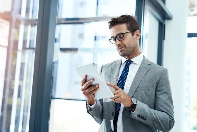 Professional man in business suit using tablet in modern office setting, promoting career opportunities in IT and technology fields.