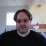 Man with glasses sitting indoors near kitchen counter