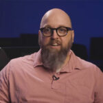 Bald man with glasses speaking on camera