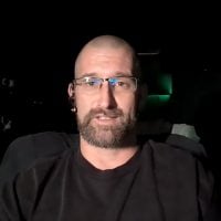 Man with glasses speaking in dark setting